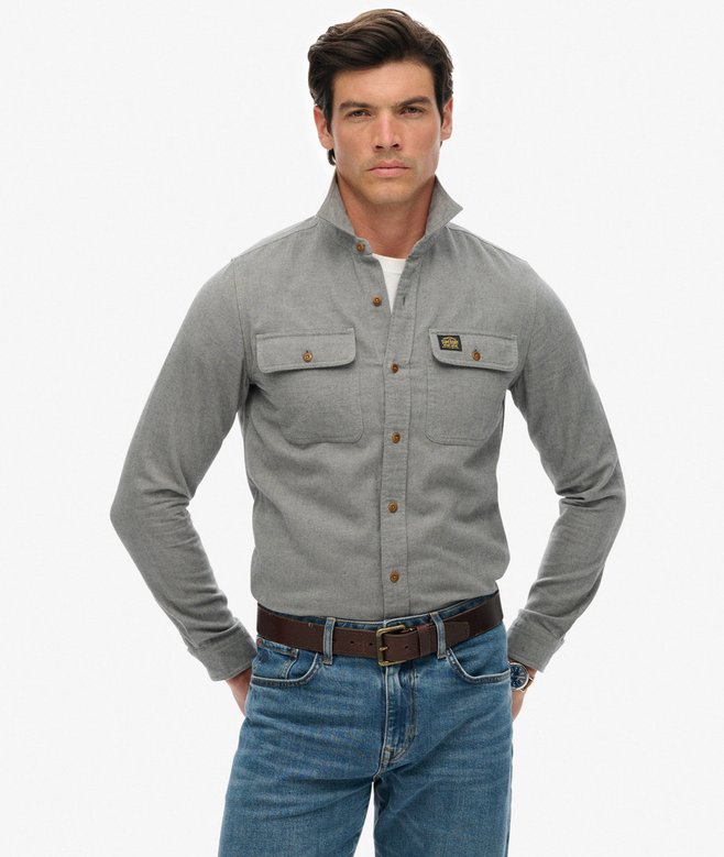 Man wearing a blue-gray shirt with button details and blue jeans on a white background