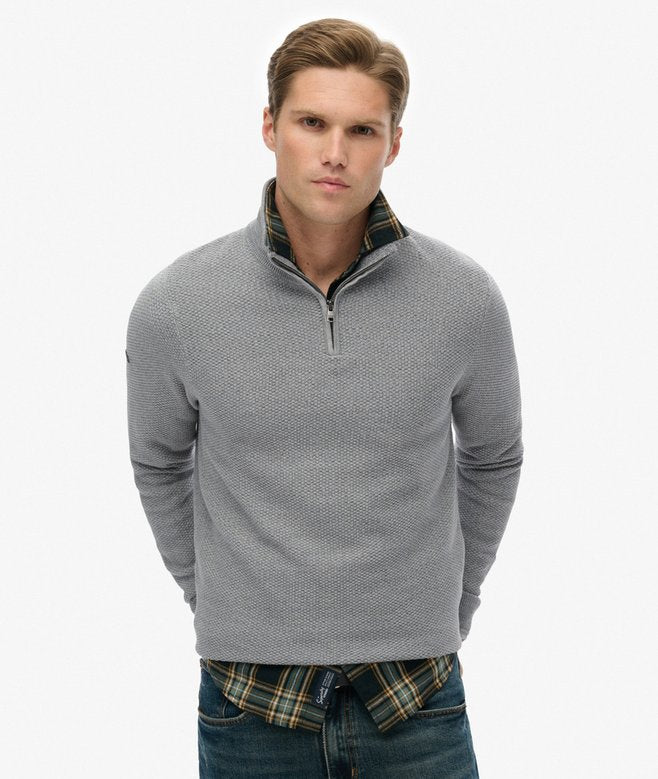 Man wearing a gray quarter-zip sweater over a plaid shirt with a white background