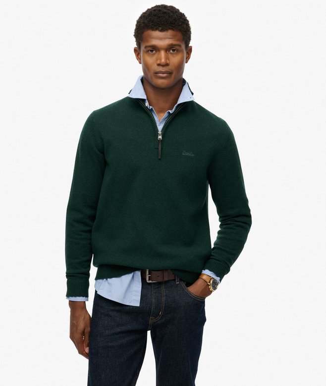 Man wearing a green quarter-zip sweater with a white shirt and dark jeans on a light gray background