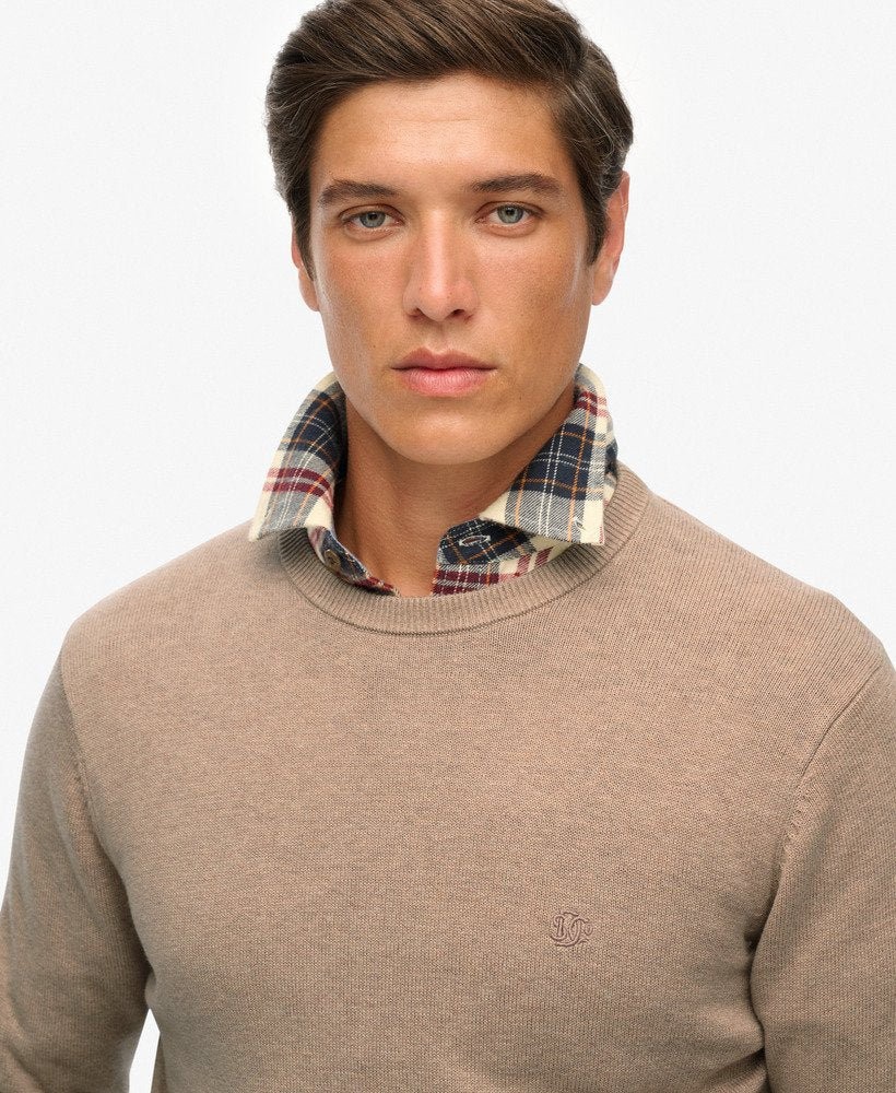 Man wearing a beige sweater with a plaid shirt underneath on a white background