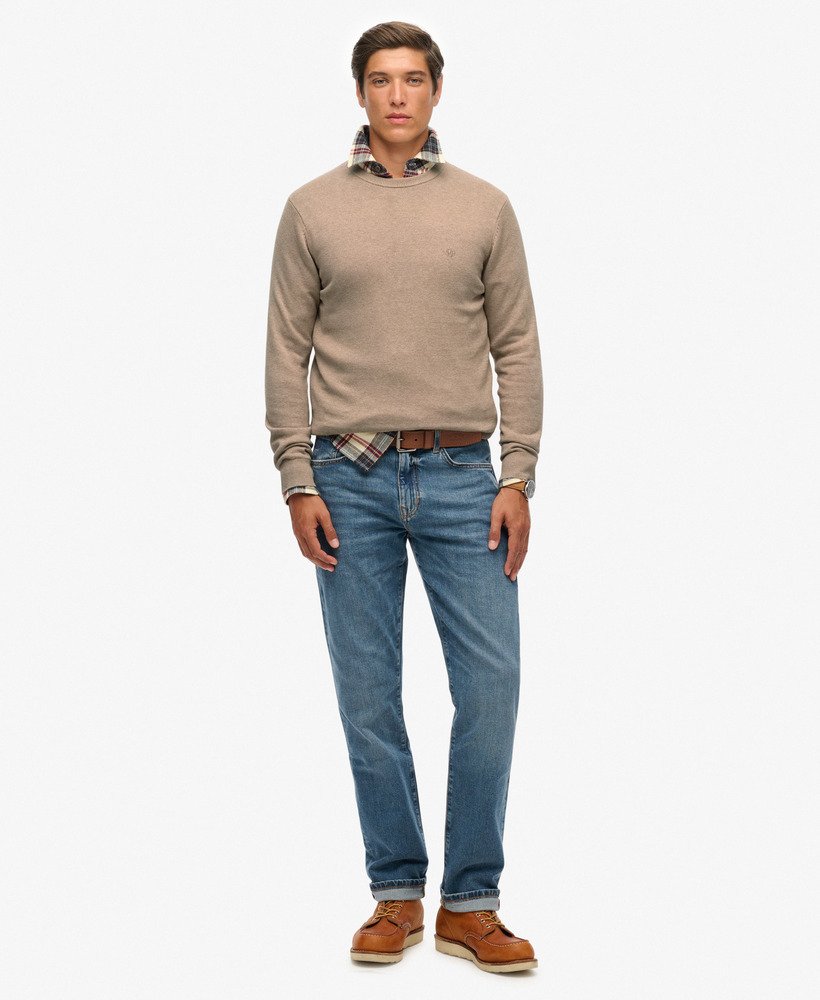 Man wearing a beige sweater, plaid shirt, blue jeans, and brown shoes on a white background