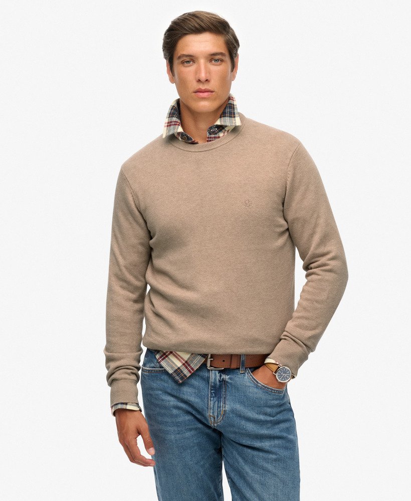 Man wearing a beige sweater with plaid collar and blue jeans on a white background