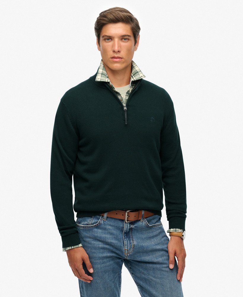 Man wearing a dark green sweater with plaid collar and blue jeans on a white background