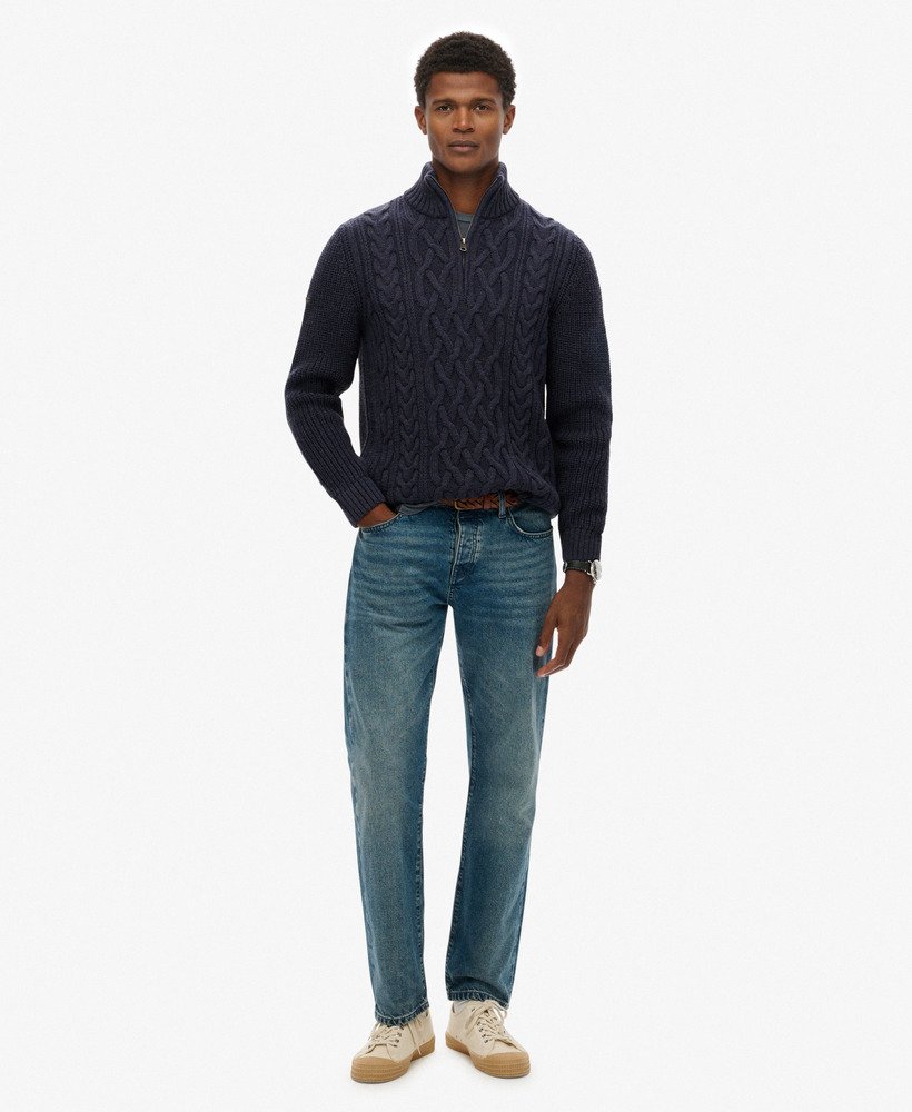 Man wearing a navy cable knit sweater and blue jeans on a white background