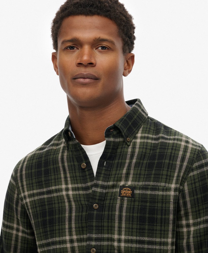 Man wearing a green plaid shirt with a Superdry logo on a white background