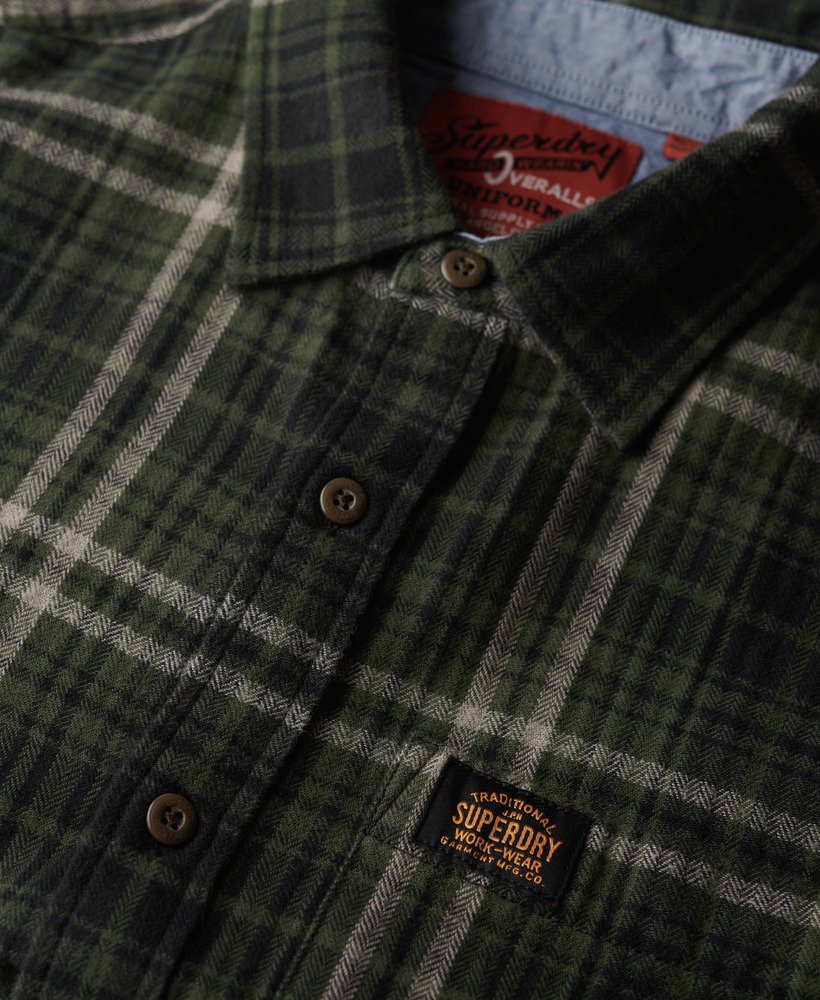 Close-up of a green plaid shirt with Superdry logo on collar and chest pocket.