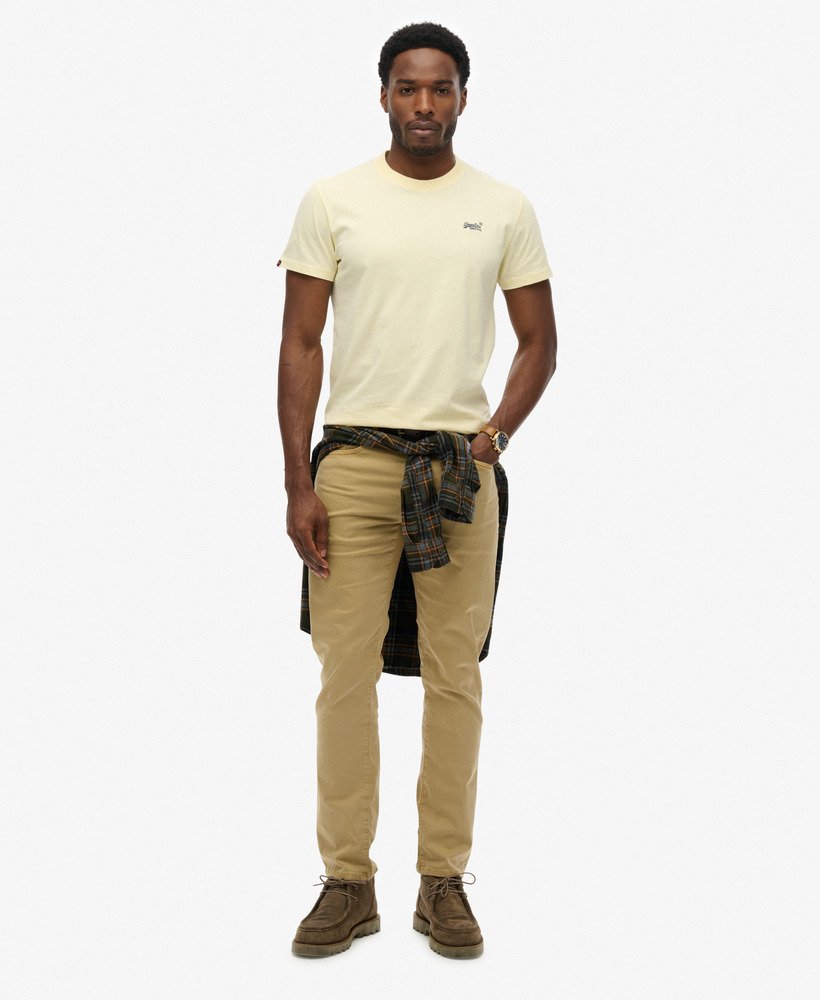Man wearing a yellow t-shirt, plaid shirt over pants, and brown boots on a white background