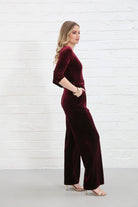 Rant & Rave Farrah Jumpsuit in wine velvet, side model view with hand in pocket and gold heels