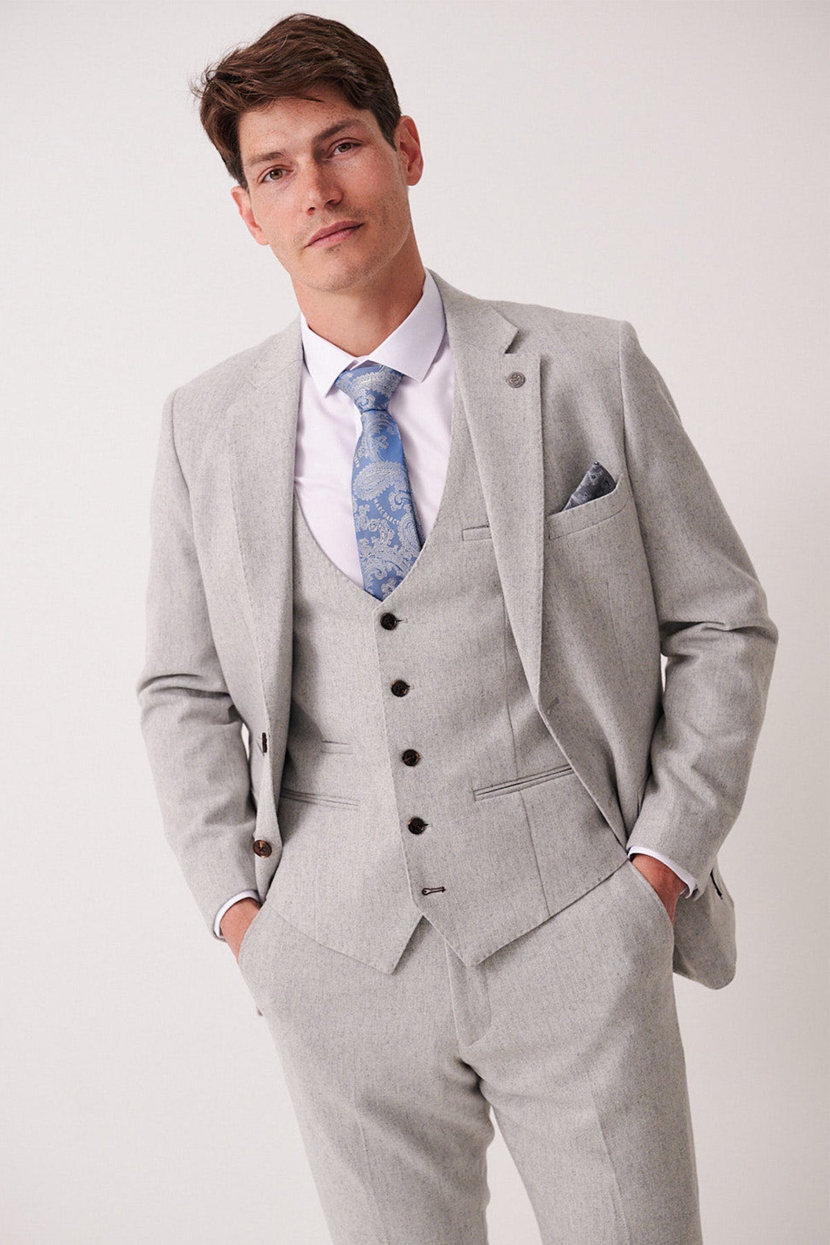 Man wearing a gray suit with a blue tie and pocket square on a white background