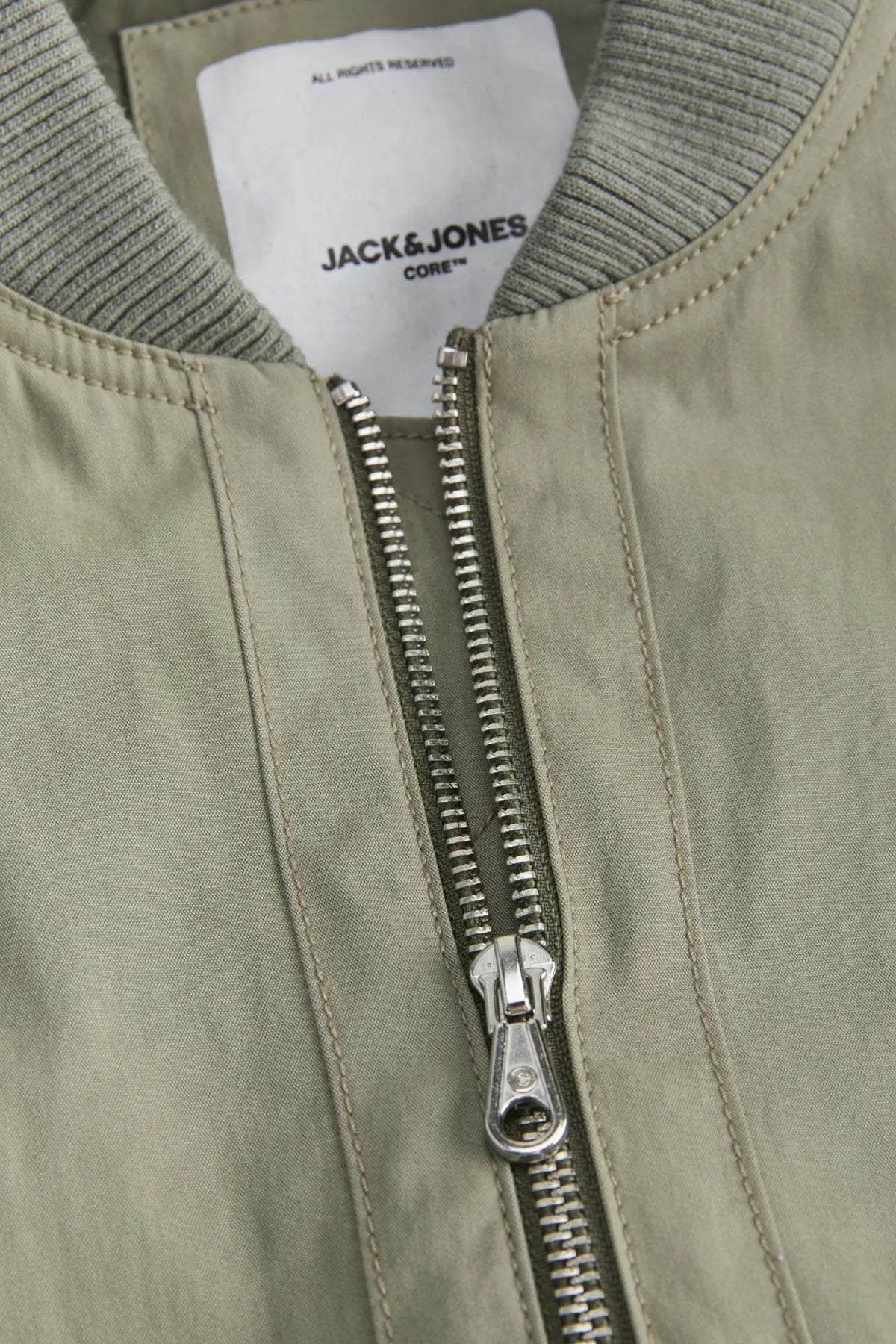 Close-up of a green bomber jacket with a silver zipper and 'Jack & Jones' label.