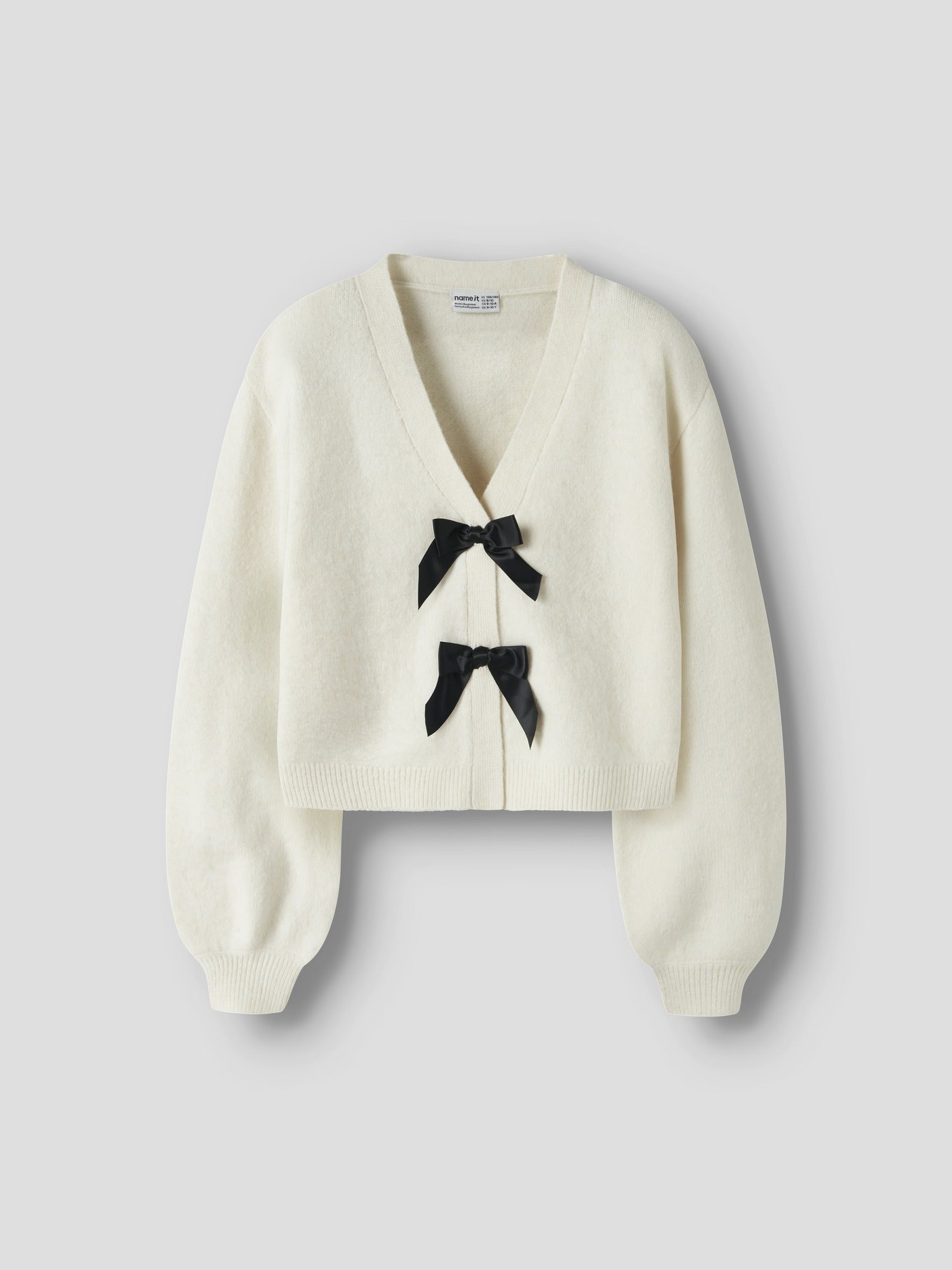 Angled view of NAME IT Rina Long Sleeve Knit Cardigan in Antique White Black Bow
