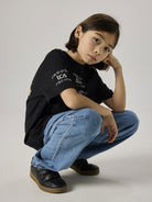 Seated model wearing the black NAME IT Alp Formula E racing T-shirt