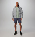 Man wearing a gray fleece jacket, green shirt, and dark shorts on a white background