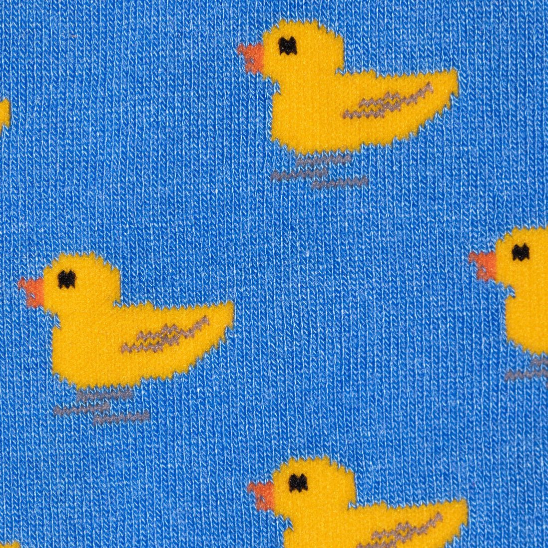 A close-up of a blue knit fabric with a repeating pattern of yellow ducklings, each with a small orange beak and black eyes.