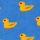 A close-up of a blue knit fabric with a repeating pattern of yellow ducklings, each with a small orange beak and black eyes.