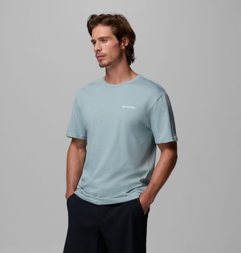 Man wearing a light blue t-shirt with a logo on a gray background