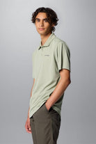 Person wearing a light green polo shirt with a brand logo on a gray background