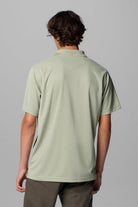 Person wearing a light green polo shirt on a gray background