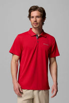 Man wearing a red polo shirt with a brand logo on a gray background
