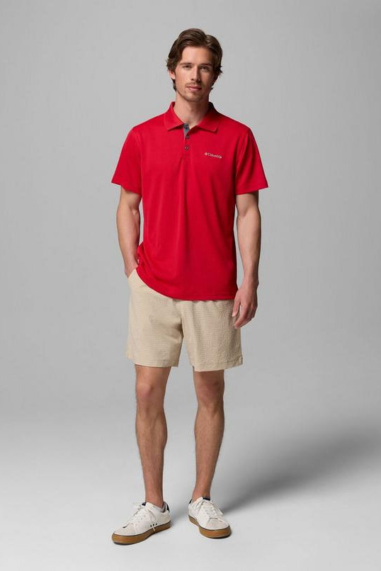 Man wearing a red polo shirt and beige shorts on a gray background