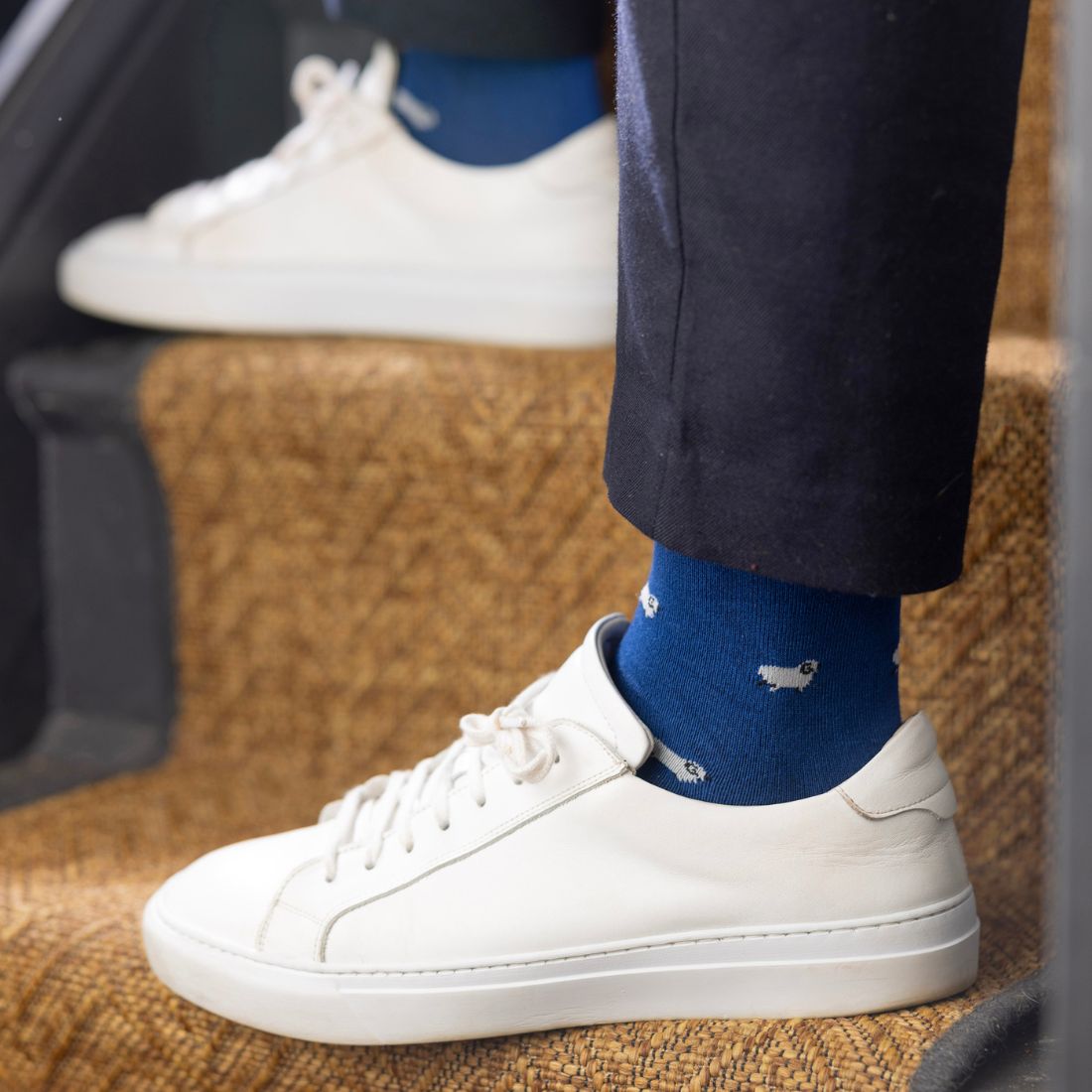 Person wearing white sneakers and blue socks with a sheep pattern, sitting on a staircase