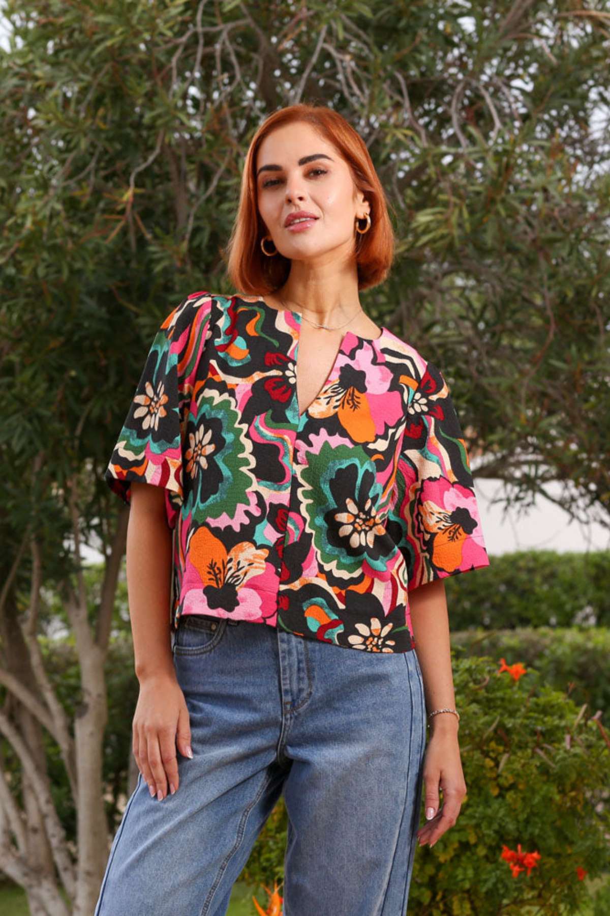 Woman wearing a colorful floral blouse and blue jeans outdoors.