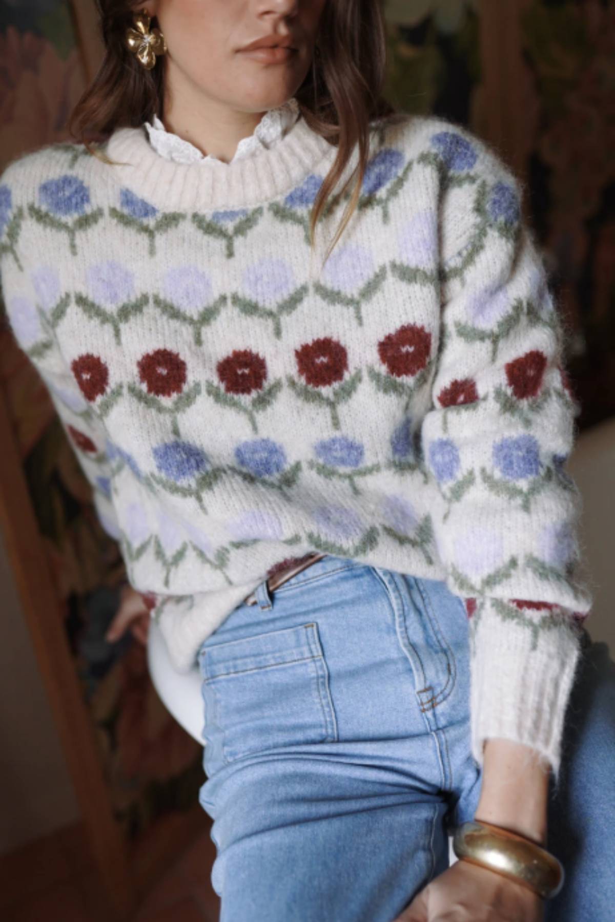 Person wearing a floral-patterned sweater and blue jeans indoors.