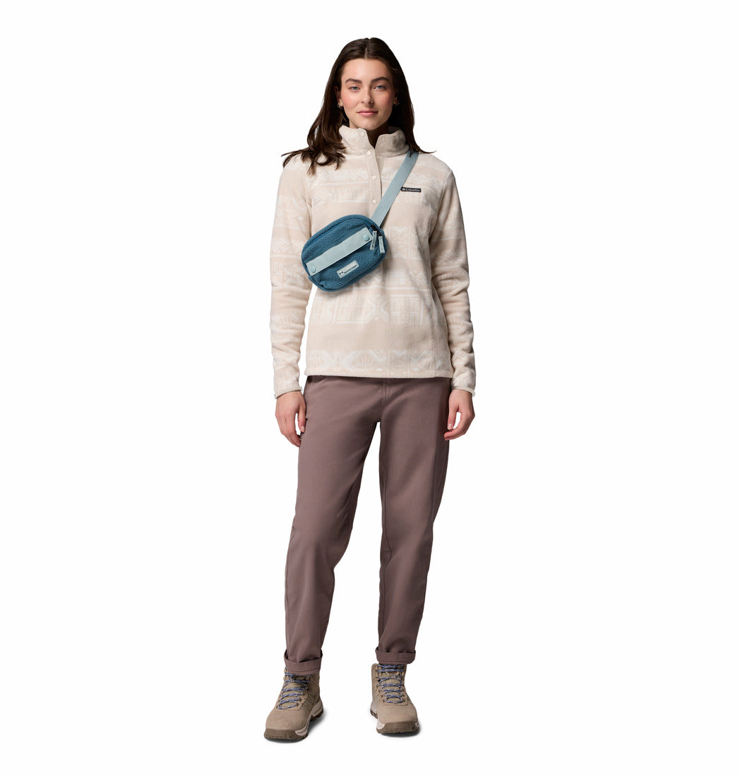 Woman wearing a beige sweater and brown pants with a blue crossbody bag on a white background