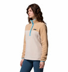 Woman wearing a beige and blue pullover with a visible brand logo on a white background