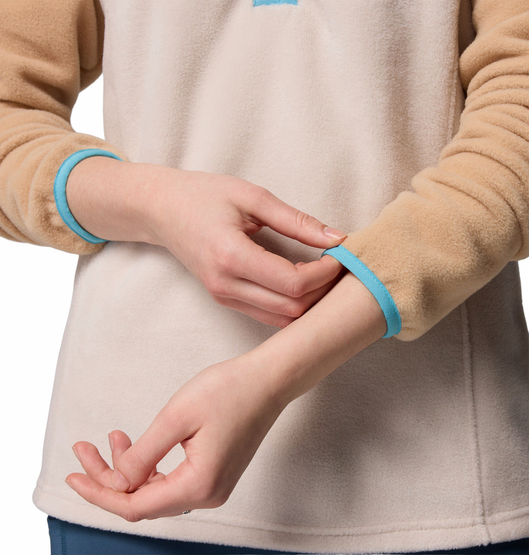 Person wearing a beige fleece jacket with blue cuffs on a plain background