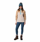 Person wearing a beige and blue pullover with blue leggings and brown boots on a white background