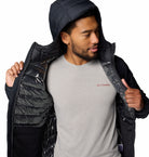 Man wearing a black puffer jacket over a gray Columbia shirt on a white background