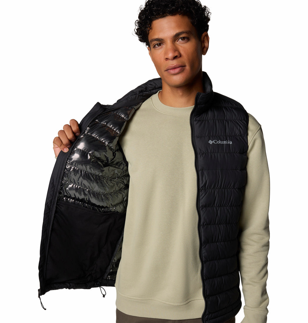 Man wearing a black puffer vest over a beige sweatshirt on a white background