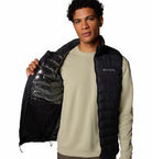 Man wearing a black puffer vest over a beige sweatshirt on a white background