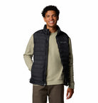 Man wearing a black puffer vest over a green shirt on a white background