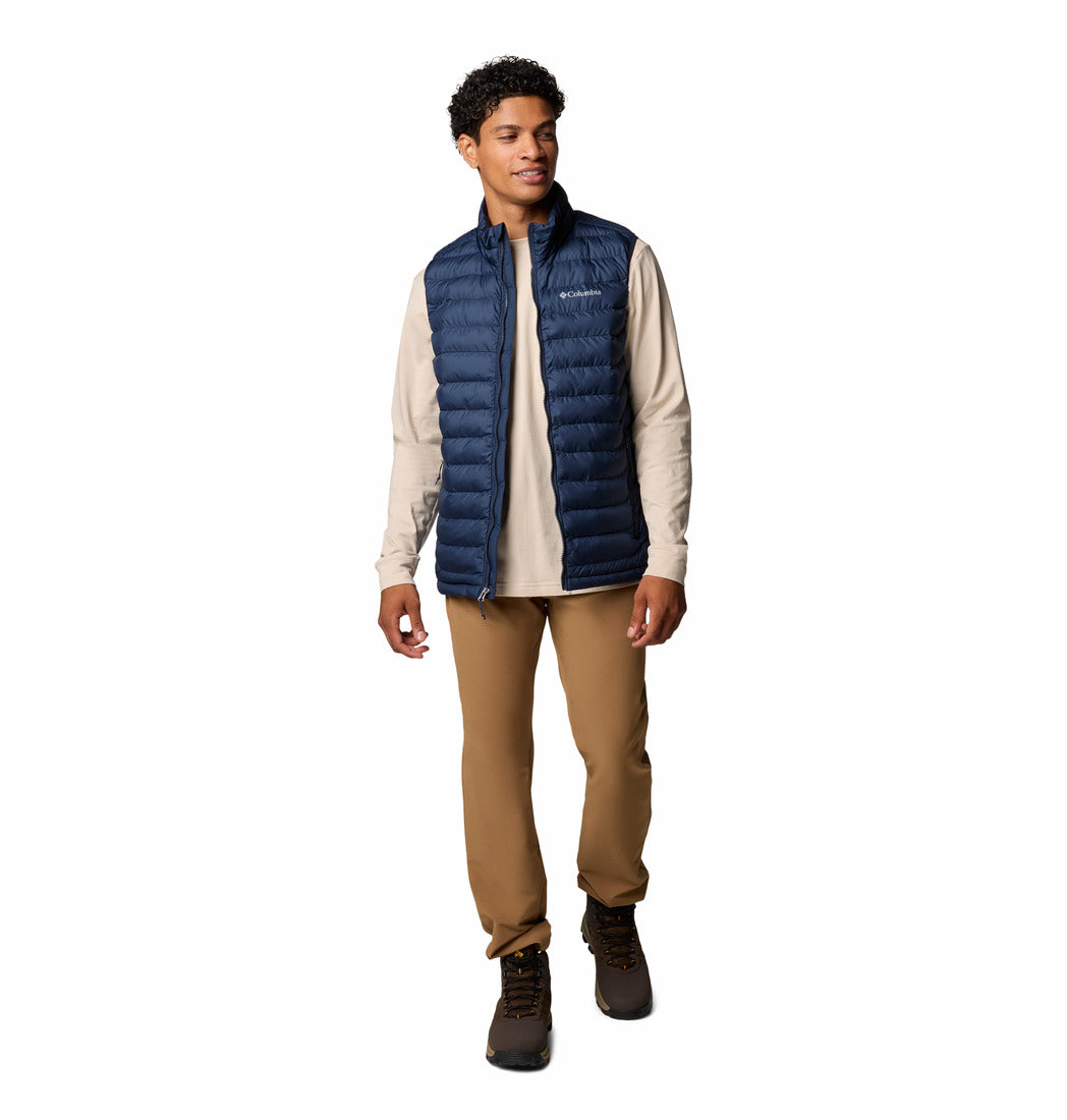 Person wearing a blue puffer vest over a beige shirt with brown pants on a white background
