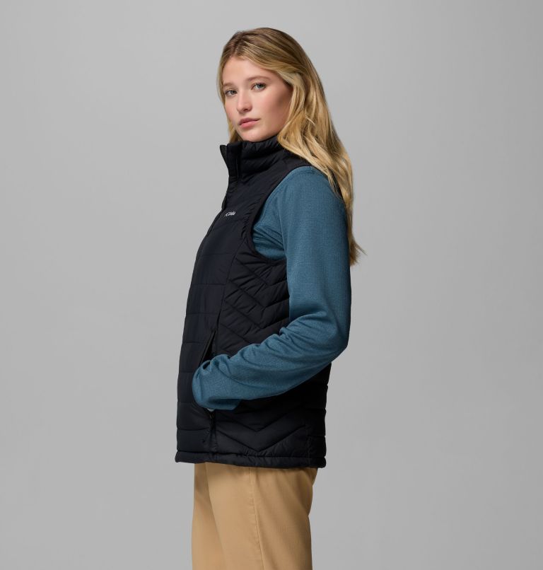Person wearing a black quilted vest over a blue jacket on a gray background