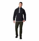 Man wearing a black pullover with a gray zipper and green pants on a white background