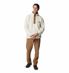 Man wearing a cream-colored pullover with a brown zipper and tan pants on a white background