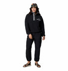 Person wearing a black outfit with a hood and colorful bucket hat on a white background