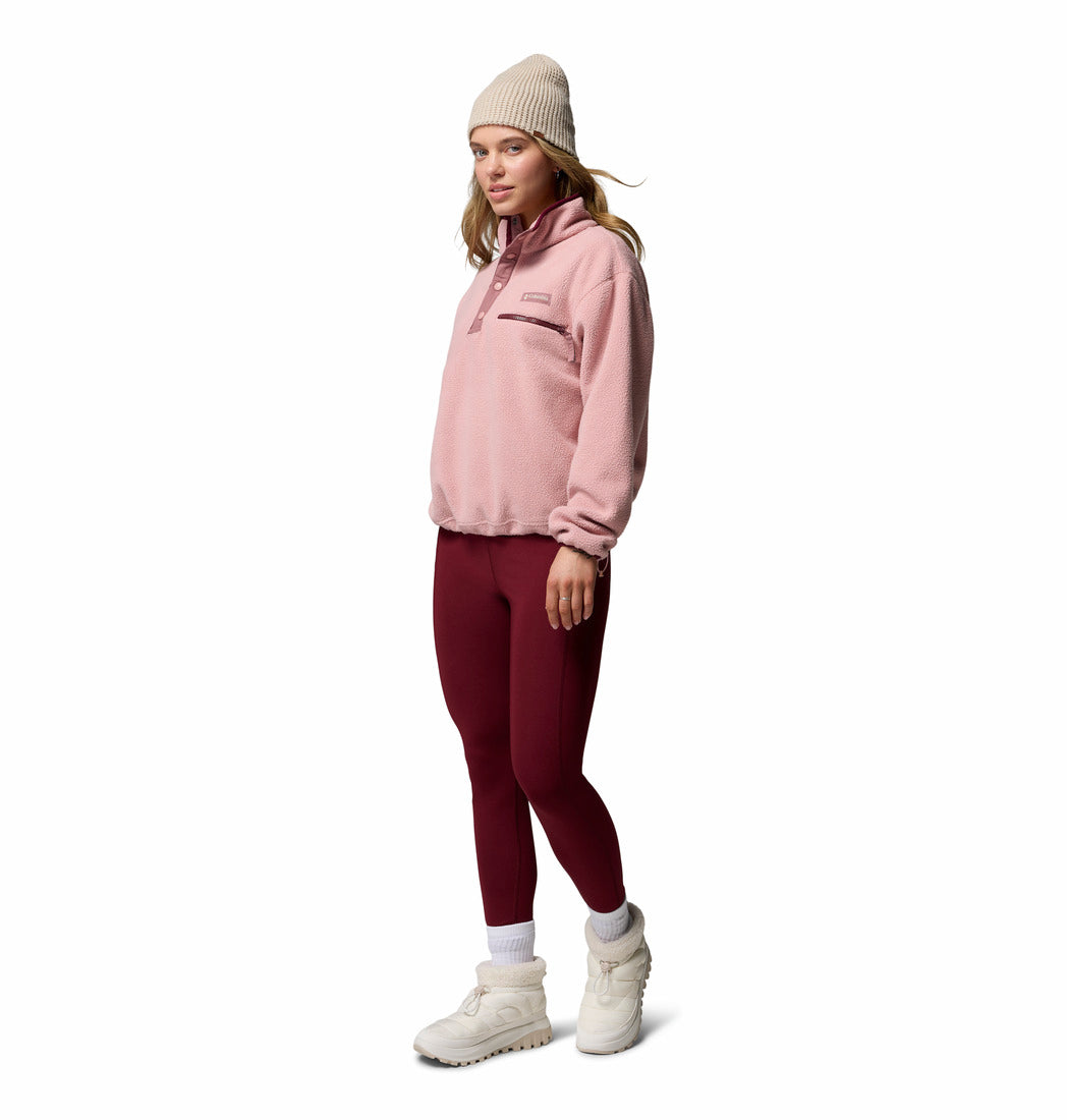 Woman wearing a pink fleece pullover, maroon leggings, white beanie, and white boots on a white background