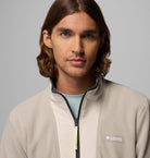 Man wearing a beige fleece jacket with Columbia logo on a gray background