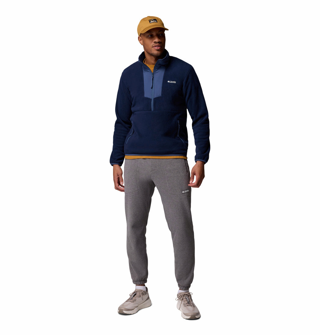 Man wearing a navy pullover, gray jogger pants, and a yellow cap on a white background