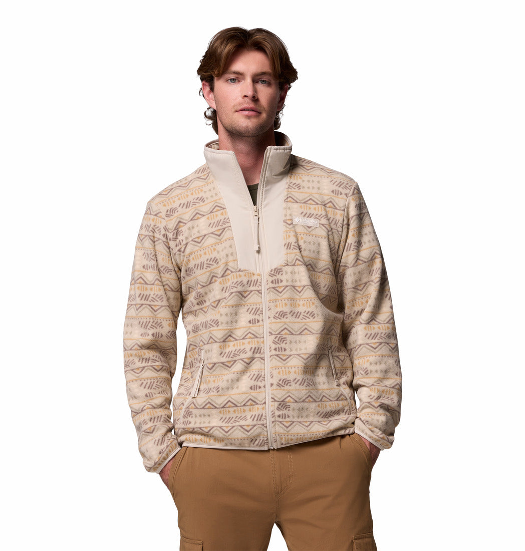 Man wearing a patterned beige jacket and brown pants on a white background