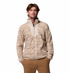 Man wearing a patterned beige jacket and brown pants on a white background