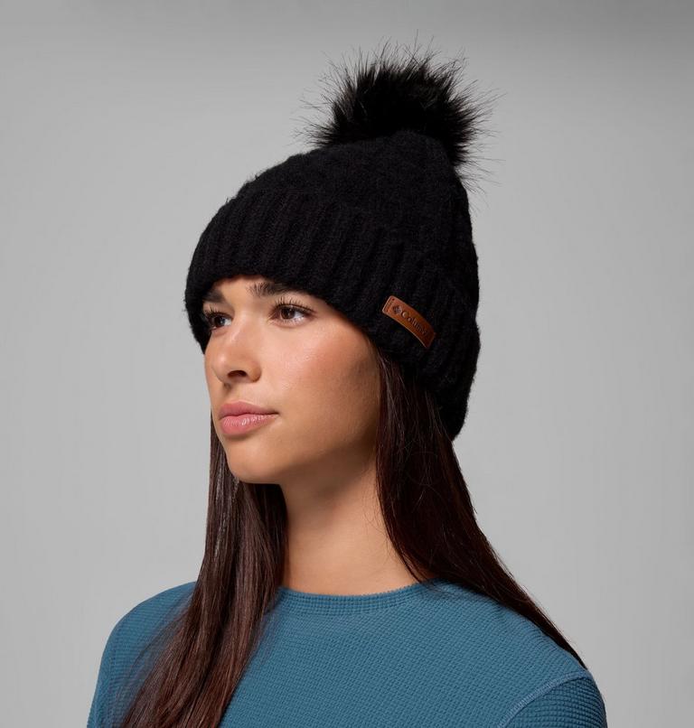 Woman wearing a black knit beanie with a pom-pom on a gray background