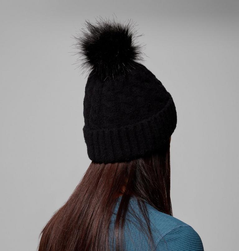 Person wearing a black knit beanie with a pom-pom on a gray background