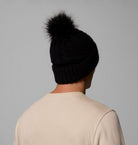 Person wearing a black beanie with a fur pom-pom on a gray background