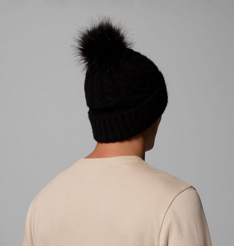 Person wearing a black beanie with a fur pom-pom on a gray background