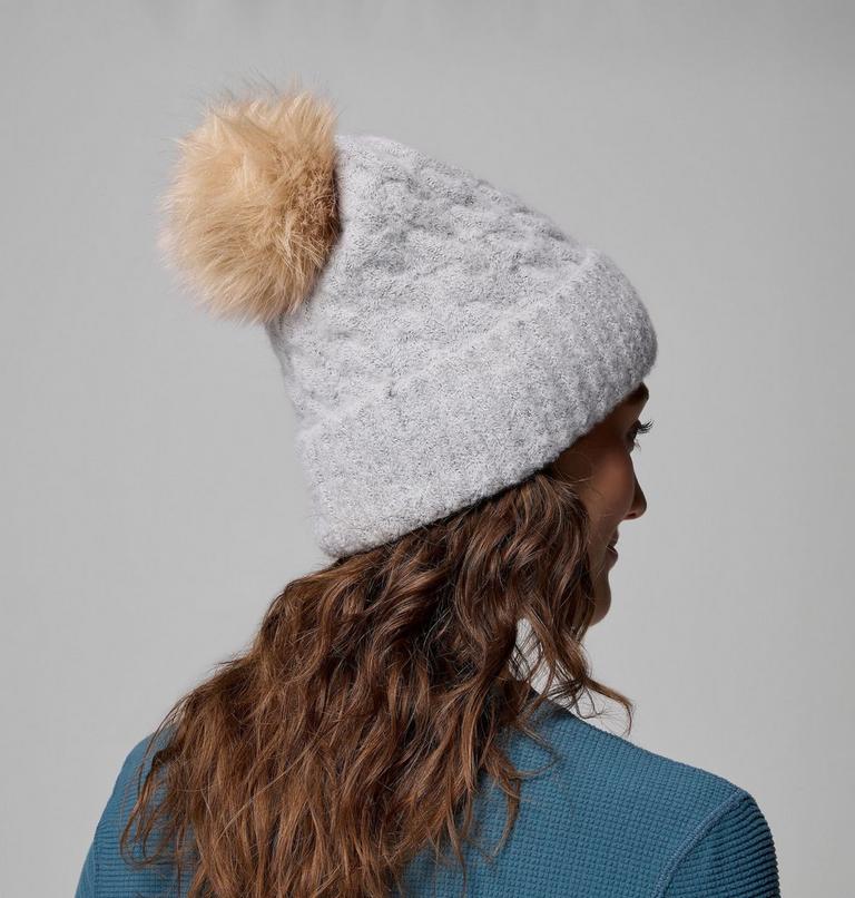 Person wearing a gray knit beanie with a brown pom-pom on a gray background